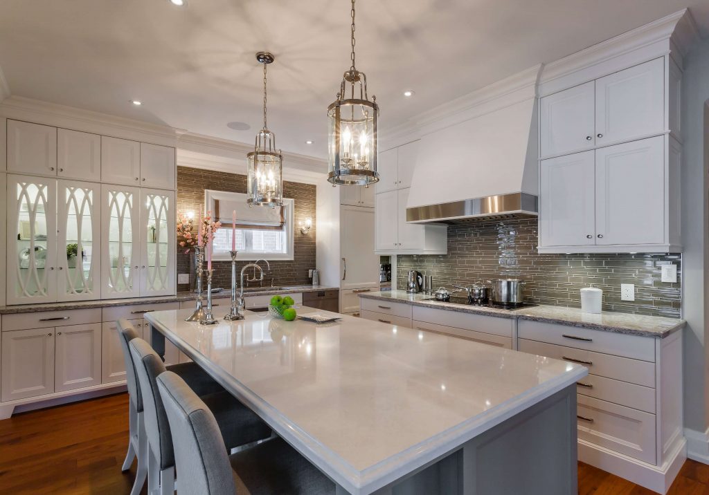 Explore homes for sale in Burlington featuring a spacious modern kitchen with a large marble island, stainless steel appliances, white cabinetry, two pendant lights, and a tiled backsplash, custom house builders, homes for sale in Burlington