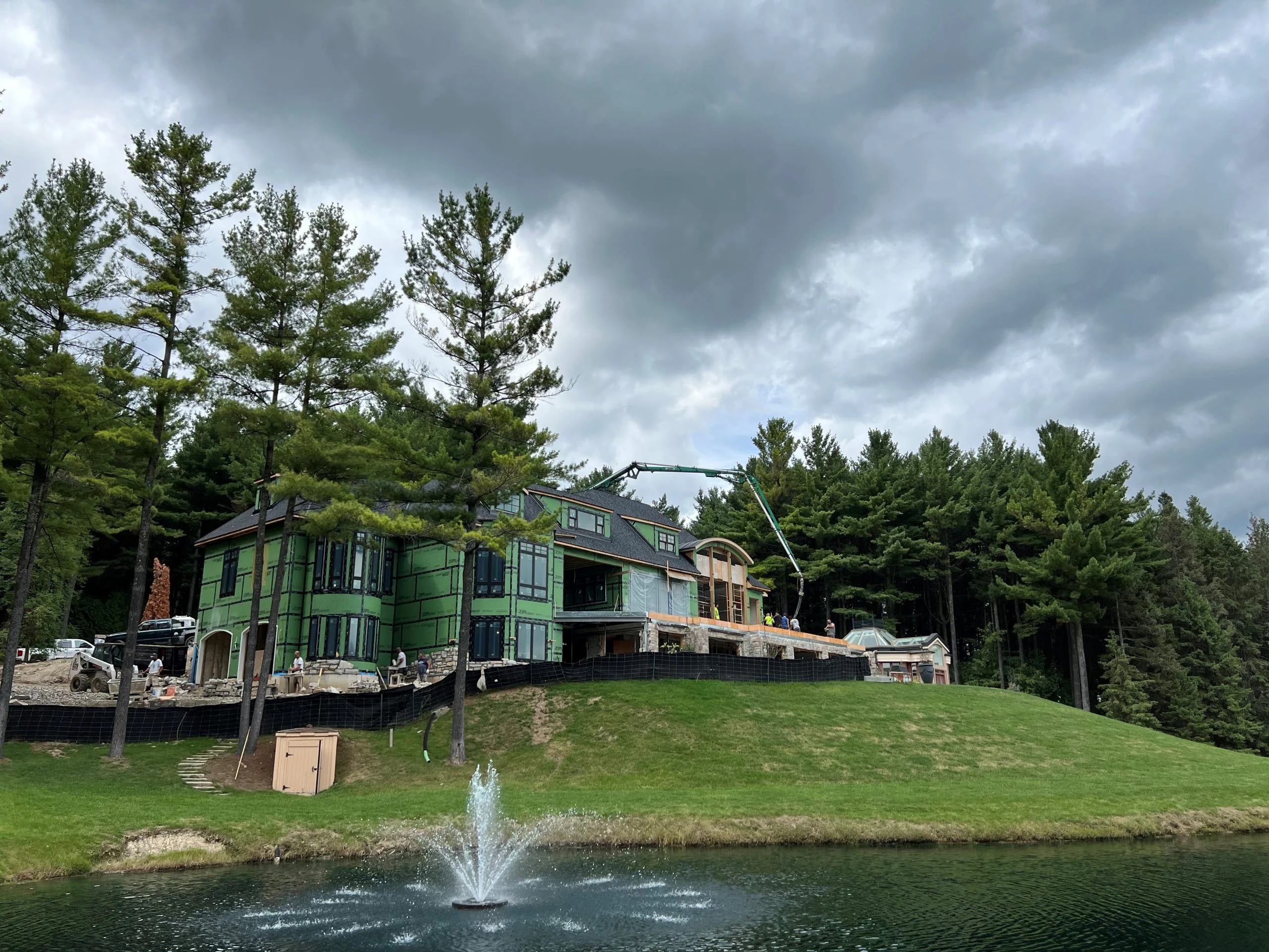 A green house with a fountain in the middle of a wooded area.