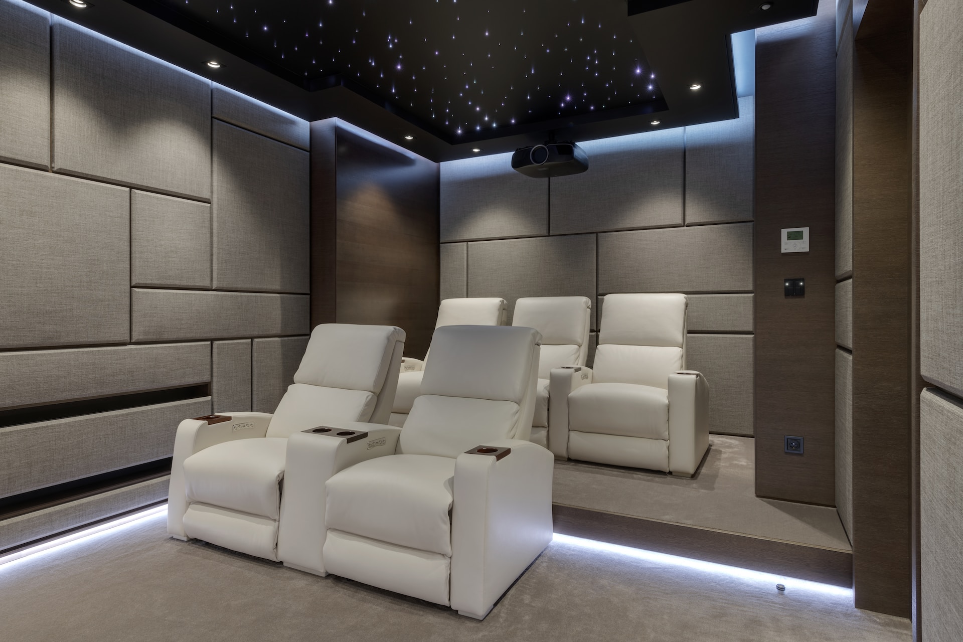 A custom luxury home theater with white recliner chairs, a starry ceiling, and wall panels on both sides, high-end luxury home builders