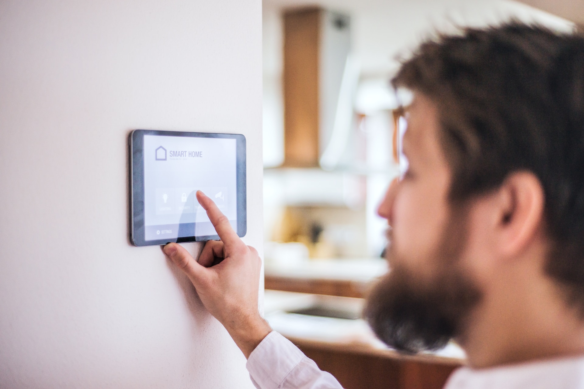 A person with a beard interacts with a smart home control panel mounted on a wall in one of these custom luxury homes.