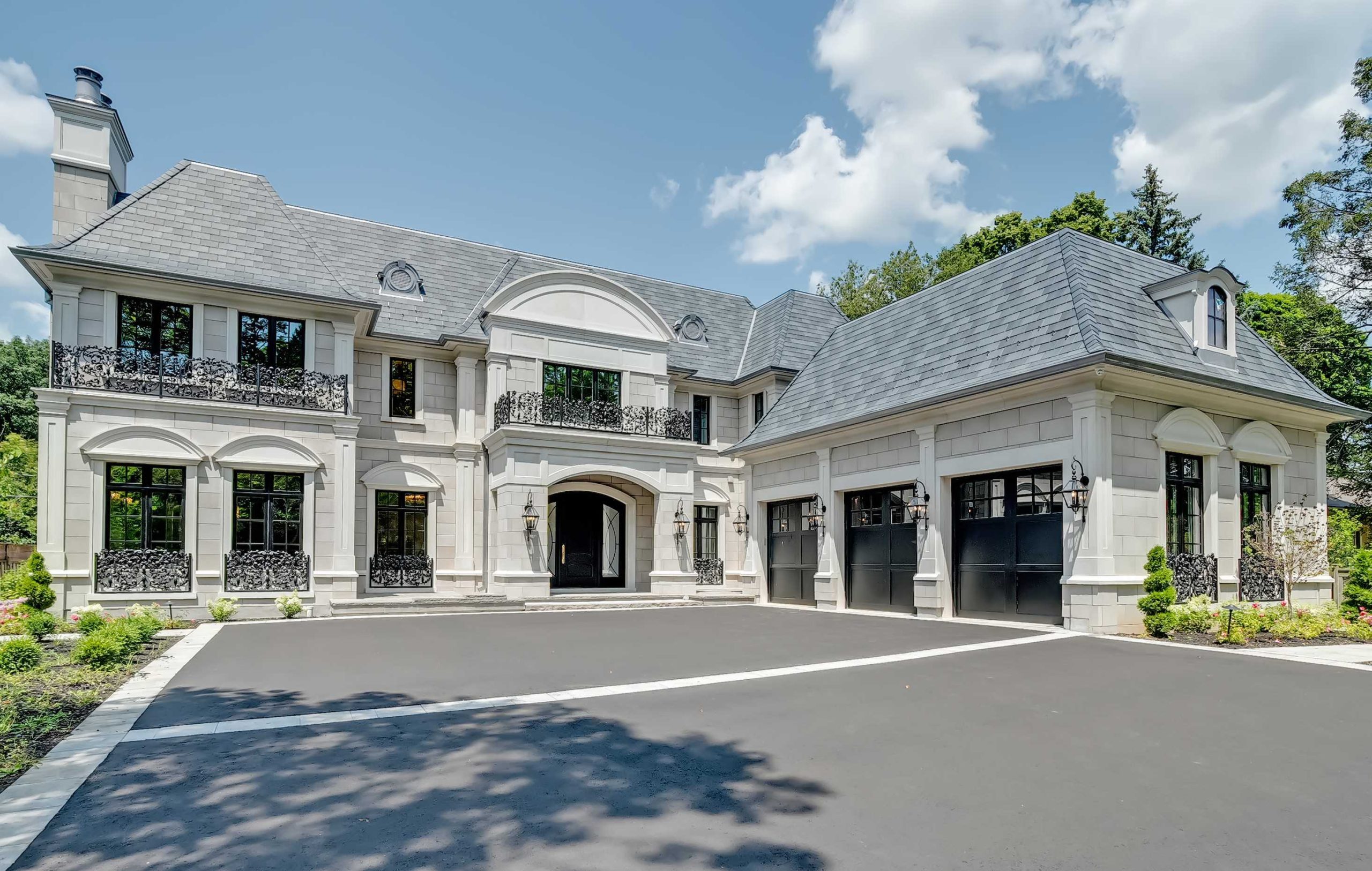 A large, two-story, European-style custom home in Oakville with a gray slate roof, arched windows, black wrought iron balconies, and a three-car garage. The exterior features light stonework and a spacious driveway.