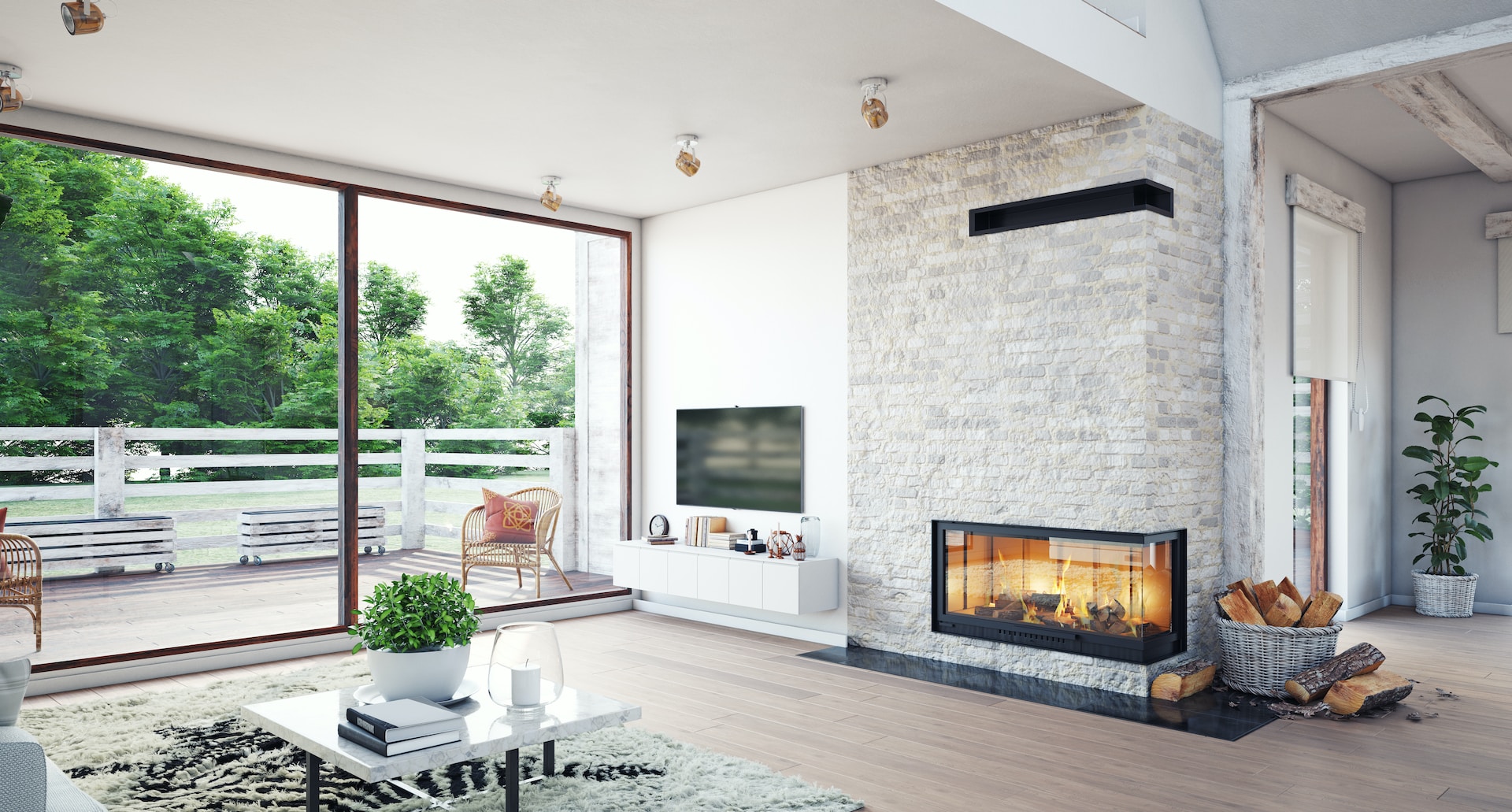 Modern living room in a luxury custom home with large glass sliding doors opening to a deck, light wood flooring, a stone fireplace, a wall-mounted TV, a coffee table with a small plant, and a basket of firewood.