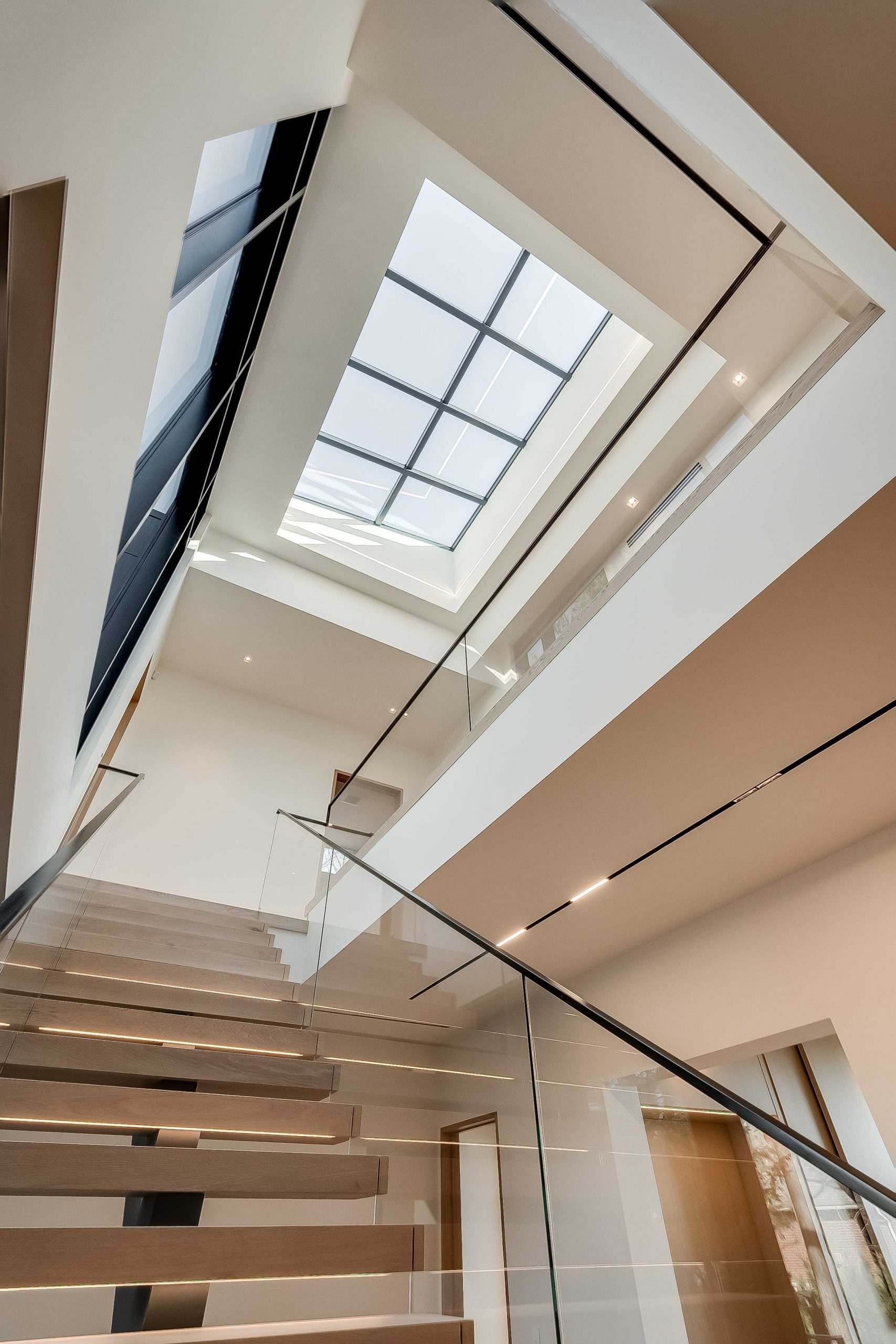 A modern staircase with glass railings and a skylight at the west Oakville lakefront., custom luxury homes