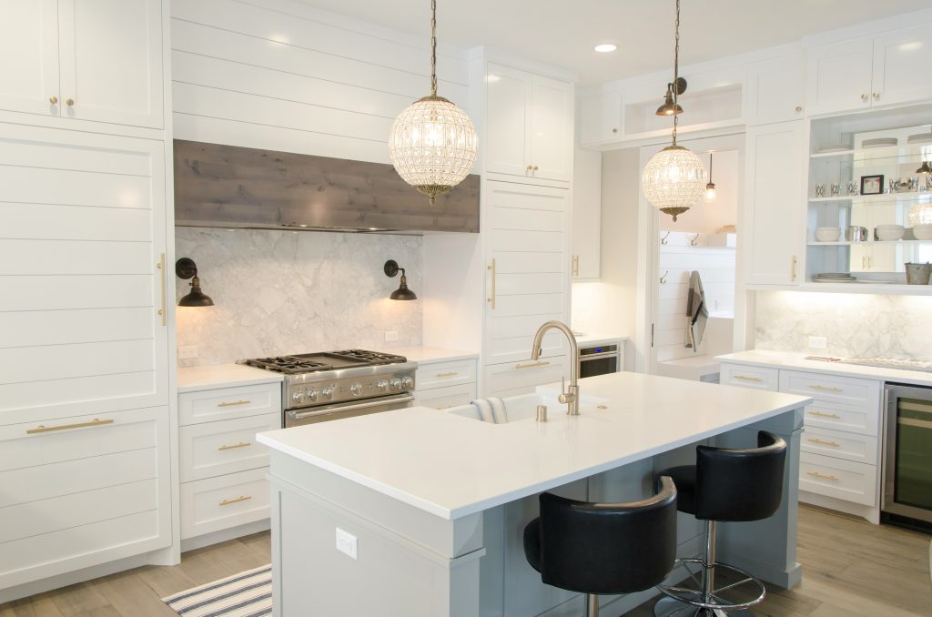 A modern kitchen in Oakville features white cabinetry, a large white island with a sink, black bar stools, stainless steel appliances, and two pendant lights hanging above the island, Kitchen Oakville