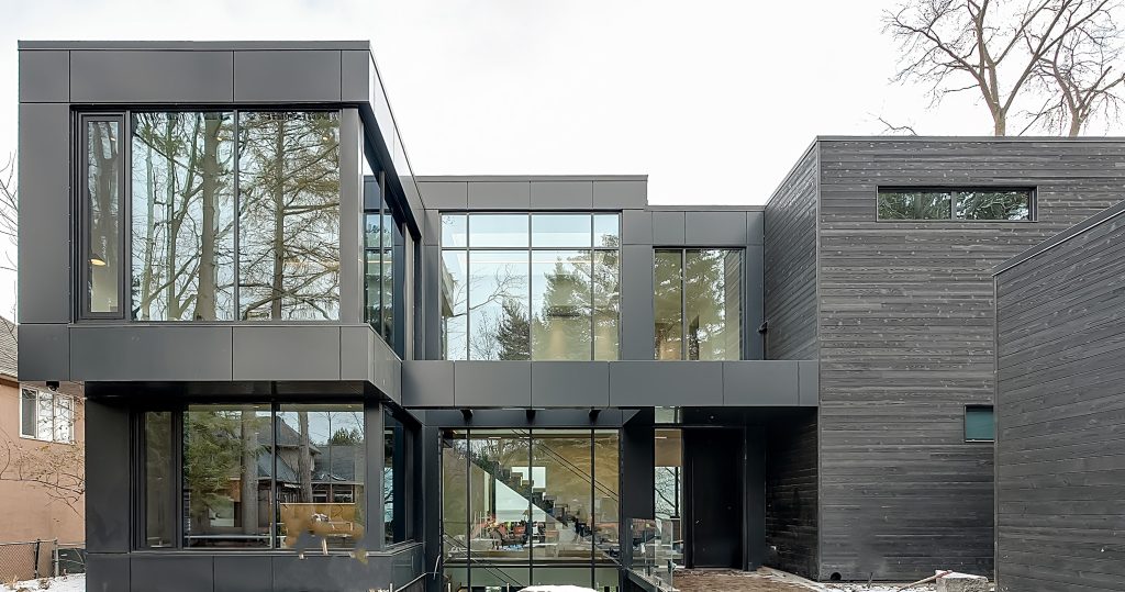 Modern two-story green building house with large glass windows and dark wood paneling.