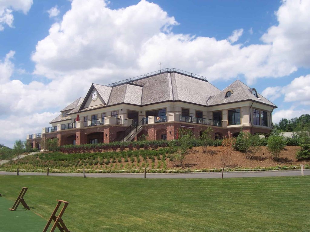 A large, two-story building with multiple gabled roofs, surrounded by landscaped greenery and a lawn, under a partly cloudy sky - the perfect location for your custom home.