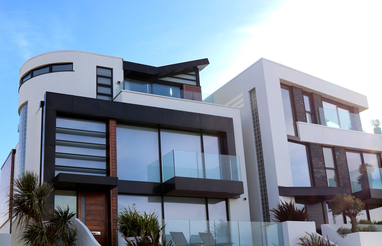 Modern multi-story building with large windows, balconies, and a flat roof, surrounded by greenery under a clear blue sky—an ideal choice among homes for sale.